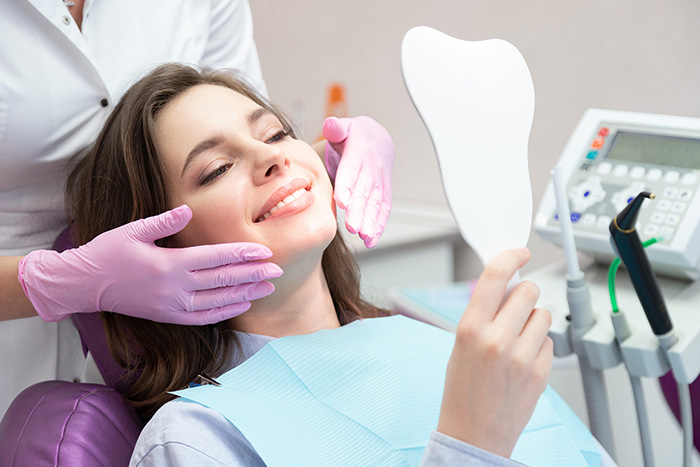 A woman admires her bright smile in the mirror after receiving teeth whitening treatment at a dental clinic.